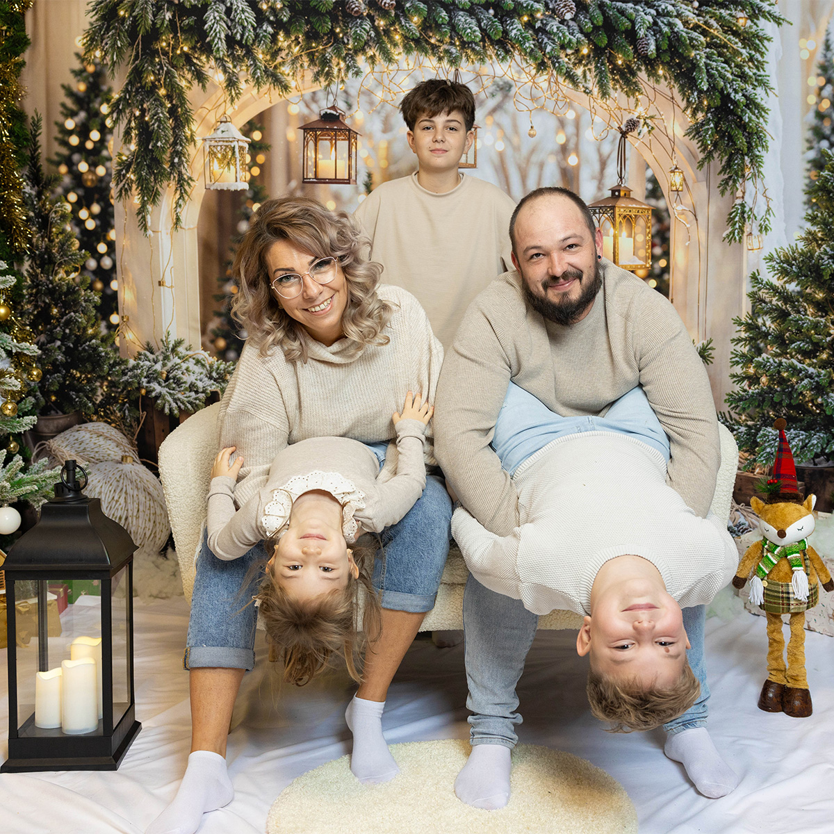 Familie fotografiată în studio într-un decor de Crăciun, cu copiii ținuți jucăuș cu capul în jos
